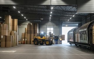 Klämtruck som lastar pappersrullar till järnvägsvagn i ett magasin.