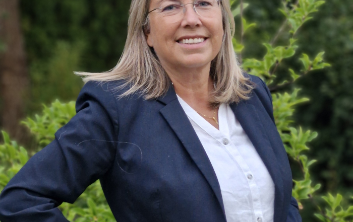 Eva Lindell, ny vd Norrköpings Hamn, kvinna, leende, i blå kavaj, grön växtlighet i bakgrunden.