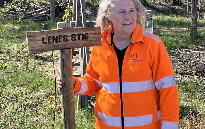 Kvinna i reflexjacka vid träskylt 'Lenes stig'