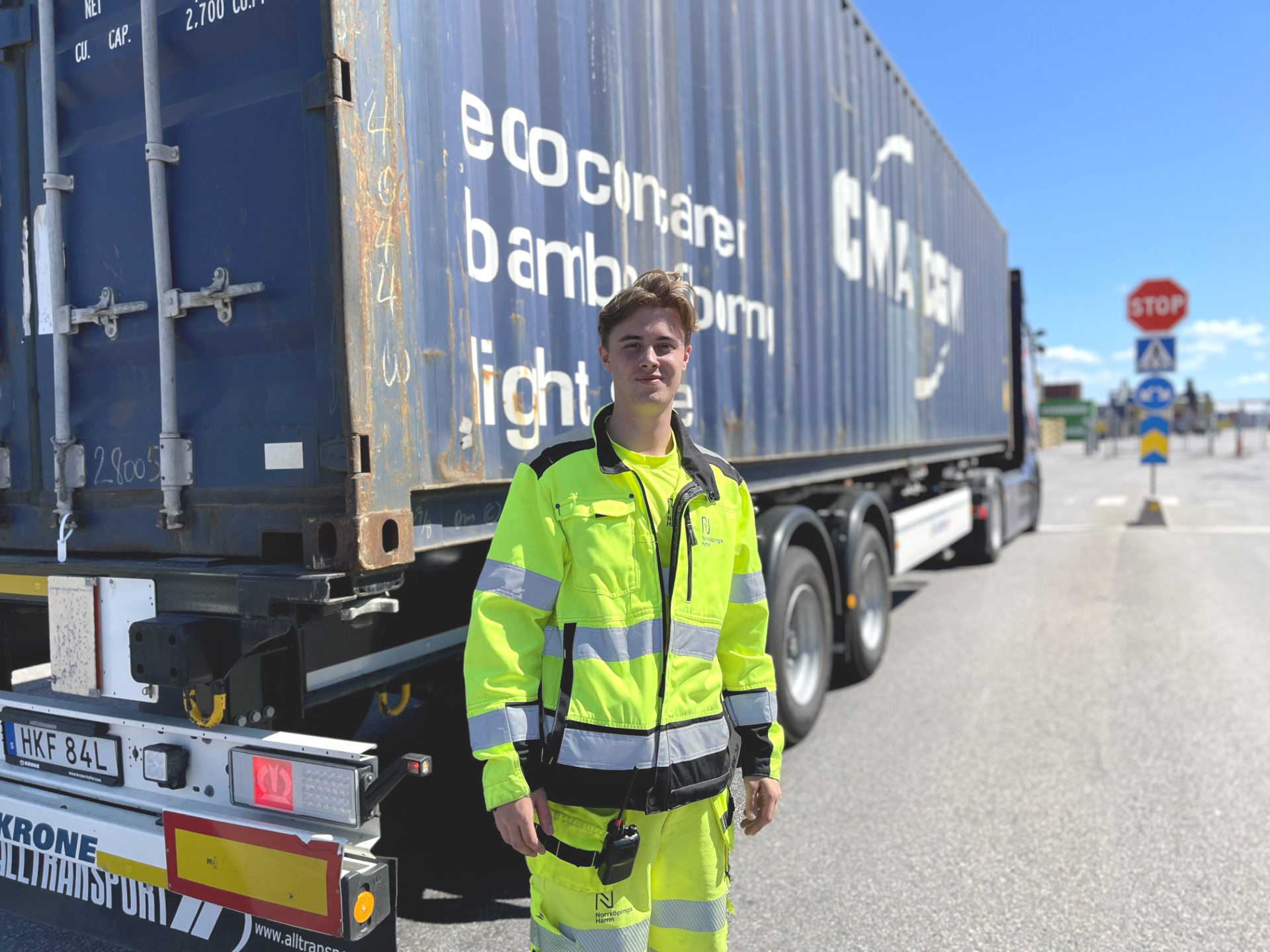 Theo Leende ung man i gula reflexkläder står framför en lastbil med en blår container.