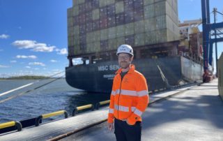 Johannes Sandgren i reflexjacka och hjälm med containerfartyg i bakgrunden.