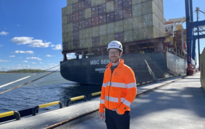 Johannes Sandgren i reflexjacka och hjälm med containerfartyg i bakgrunden.